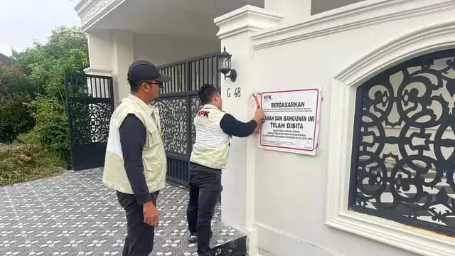 Petugas dengan rompi KPK memasang pelang penyitaan di rumah tersebut